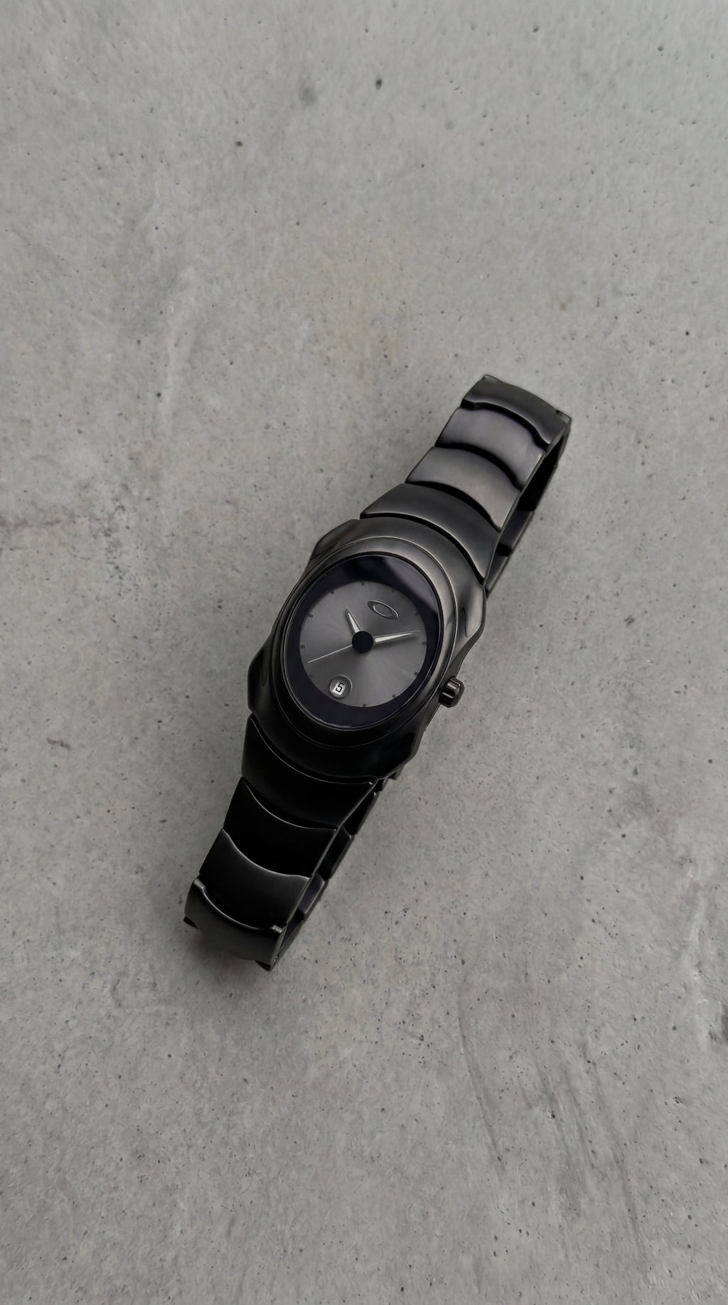Black on black Y2K, 2000s steel metal watch on a clean grey concrete surface
