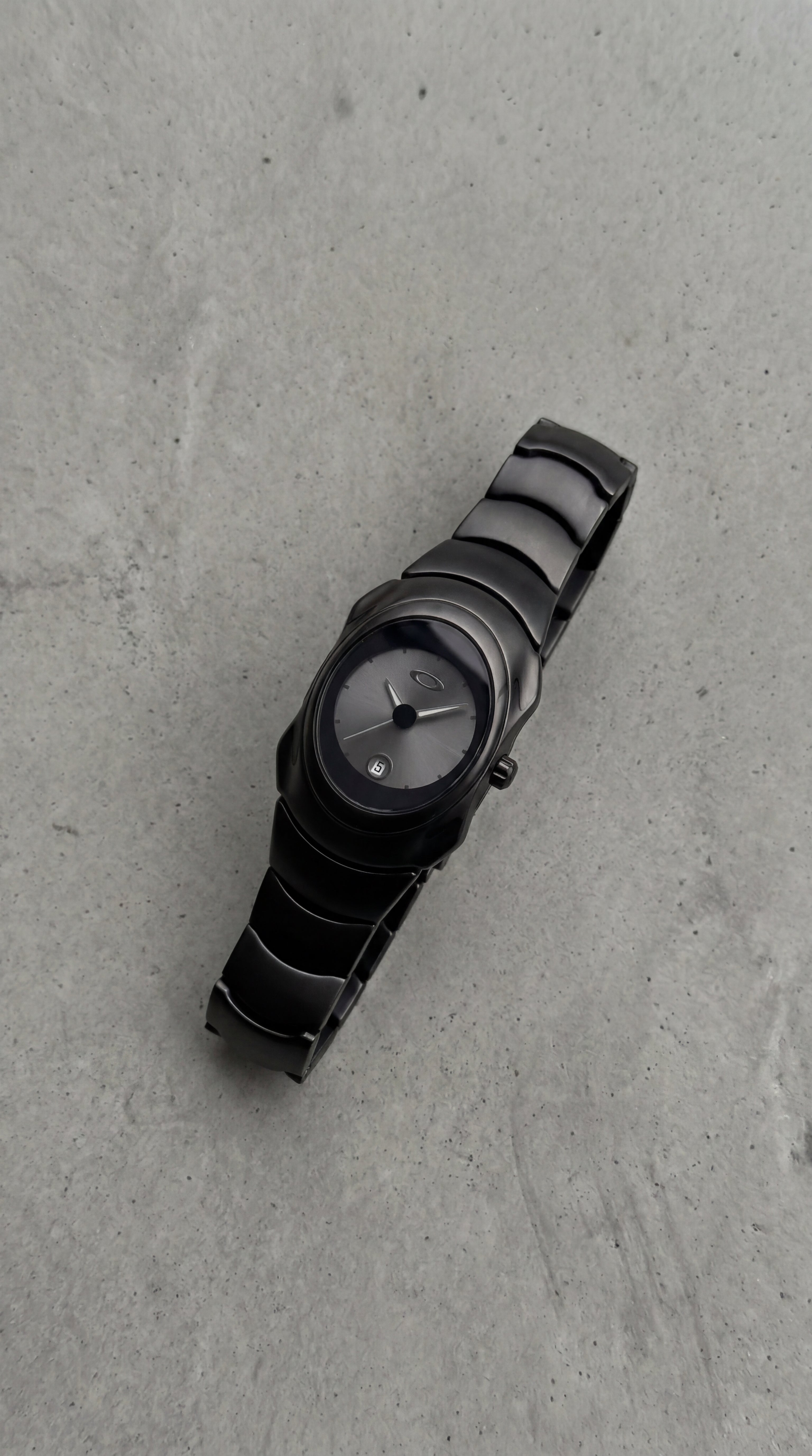 Black on black Y2K, 2000s steel metal watch on a clean grey concrete surface