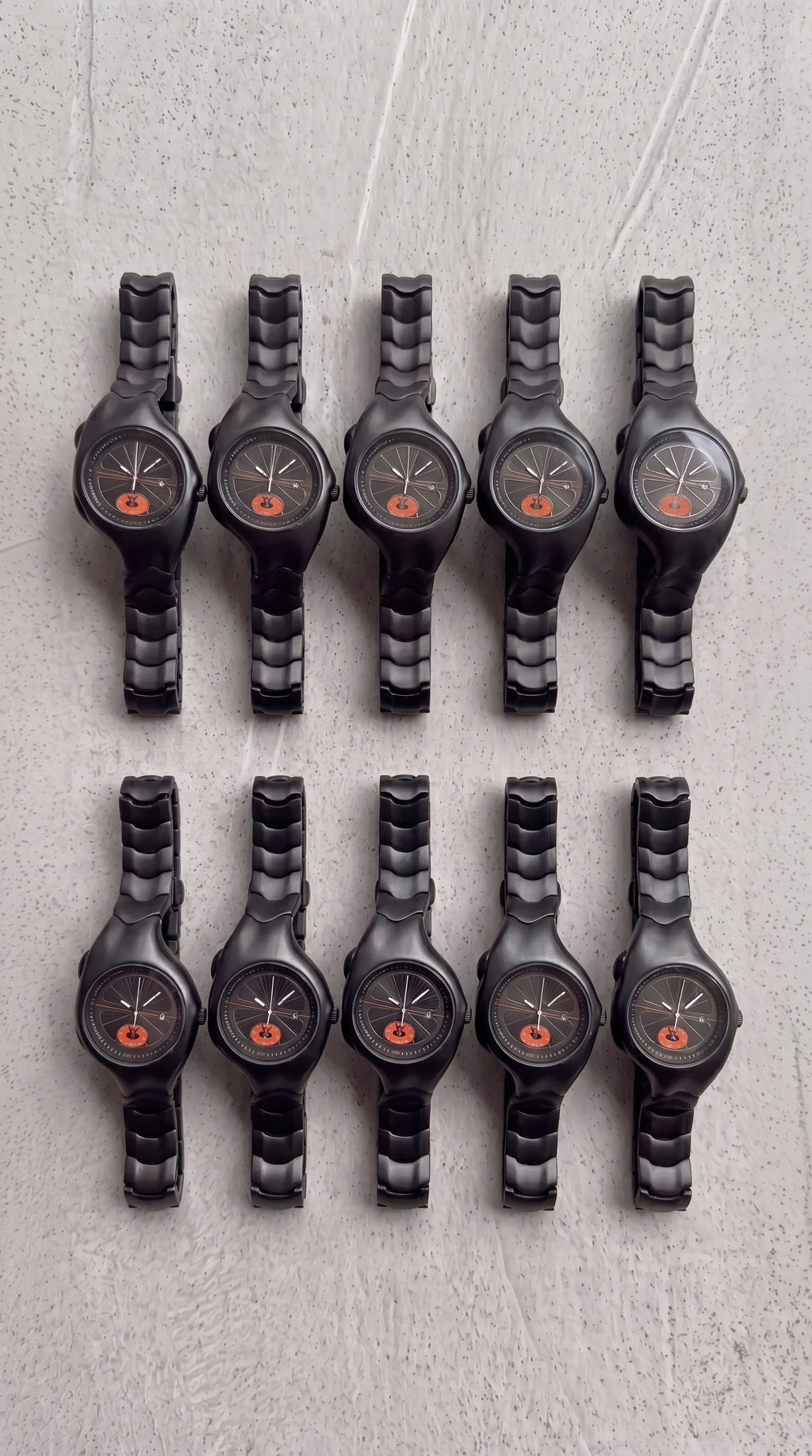 Row of black wristwatches with orange accents on a textured gray surface