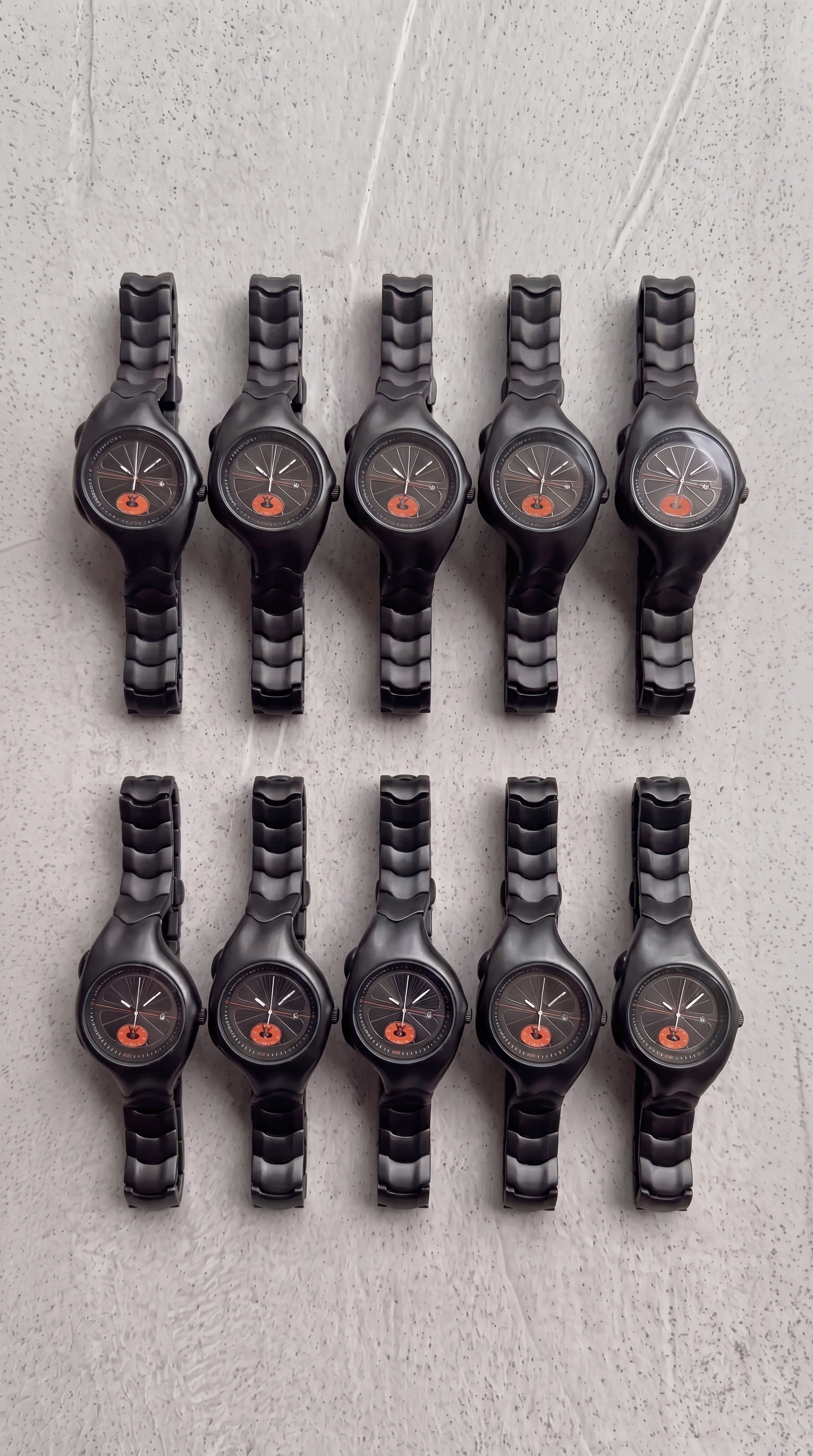 Row of black wristwatches with orange accents on a textured gray surface