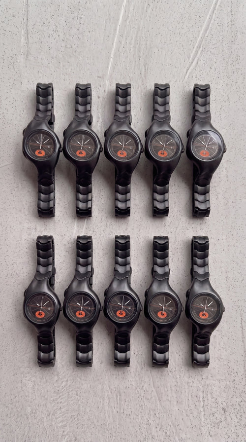 Row of black wristwatches with orange accents on a textured gray surface