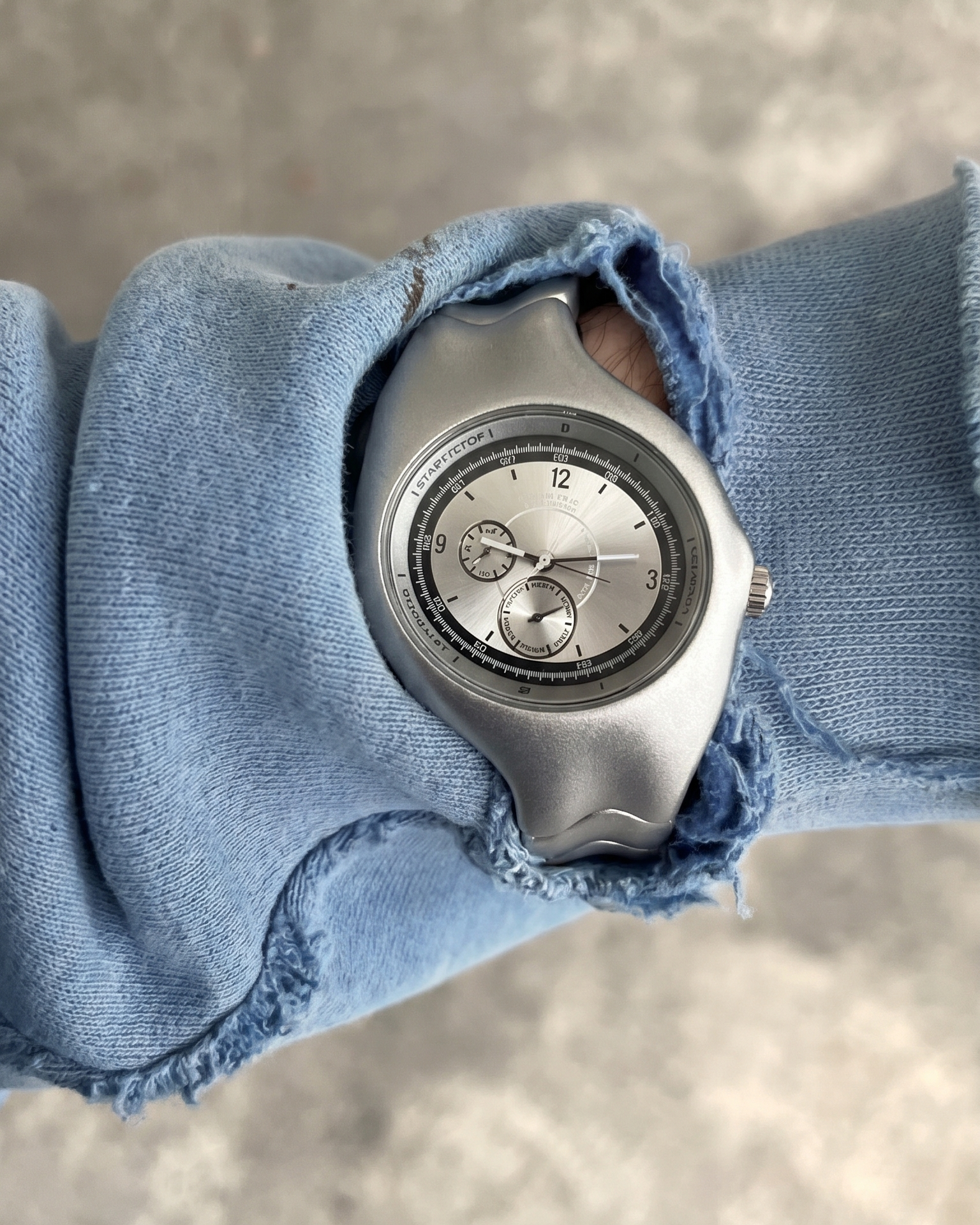 Silver Y2K watch on a wrist with denim sleeve against a gray background